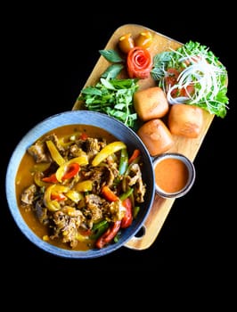 Beef stew with vegetables and banh mi bread on wooden chop board isolated on black background