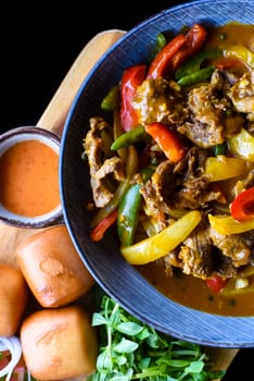 Beef stew with vegetables and banh mi bread on wooden chop board isolated on black background