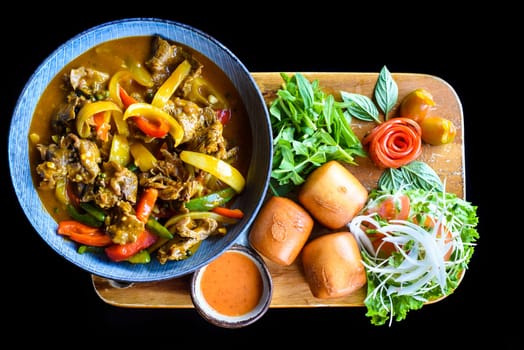 Beef stew with vegetables and banh mi bread on wooden chop board isolated on black background