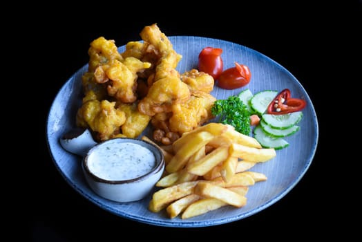 Fried frog in batter with french fries on blue plate isolated on black background top view
