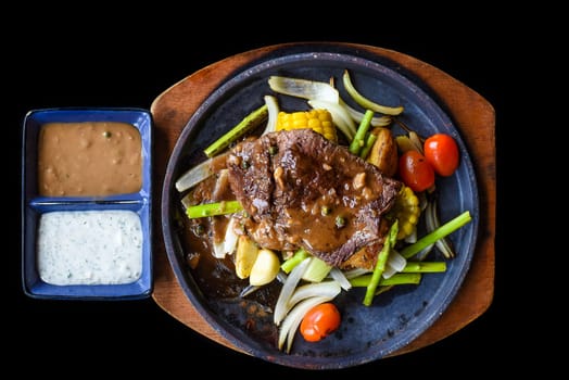 Roasted fire beef steak with vegetables and greens on plate isolated on black background top view