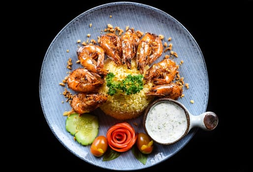 Grilled shrimps with fried rice and vegetables on blue plate isolated on black background top view