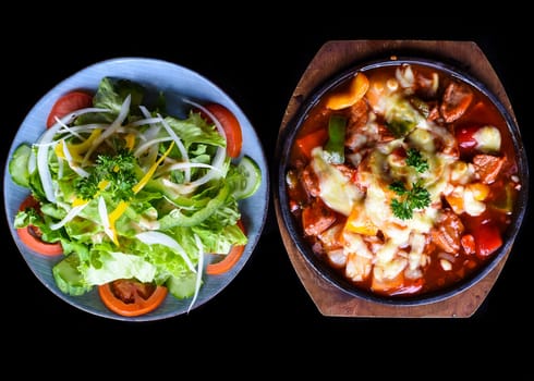 Stewed beef with cheese and vegetables on wooden plate isolated on black background side view