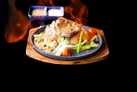 Roasted fire beef steak with vegetables and greens on plate isolated on black background side view