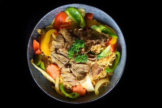Stewed beef with noodles and vegetables in a blue bowl isolated on black background top view