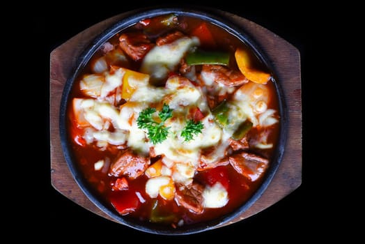 Stewed beef with cheese and vegetables on wooden plate isolated on black background top view