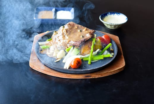 Roasted fire beef steak with vegetables and greens on plate isolated on black background side view