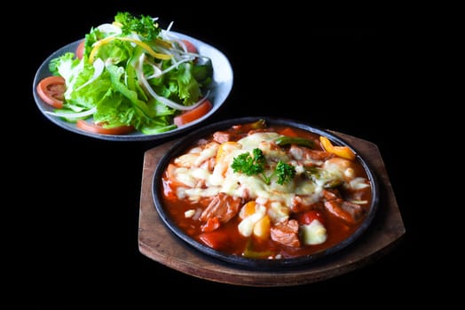 Stewed beef with cheese and vegetables on wooden plate isolated on black background side view