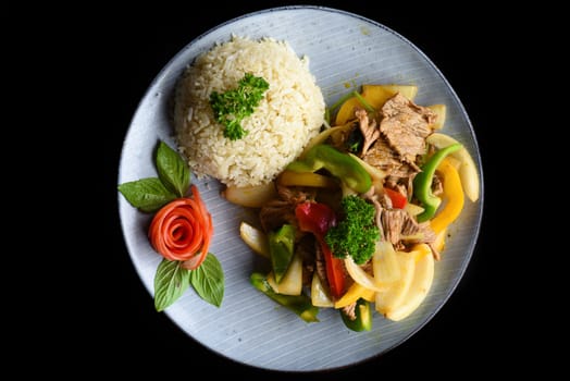 Stewed beef with vegetables with rice on blue plate isolated on black background side view