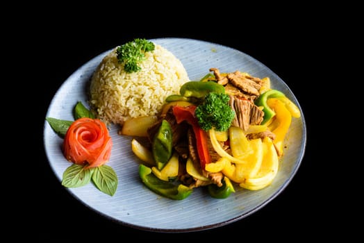 Stewed beef with vegetables with rice on blue plate isolated on black background side view