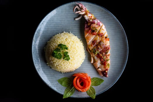 Grilled squid with white rice on blue plate isolated on black background side view