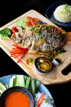 Red perch grilled in batter with vegetables and greens on wooden chop board isolated on black background side view