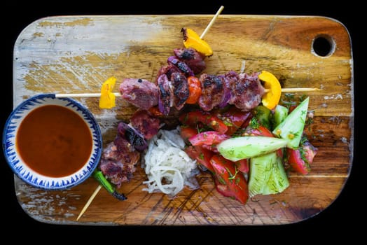 Pork skewers served with salad and sauce on black background top view