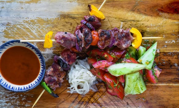 Pork skewers served with salad and sauce on black background top view