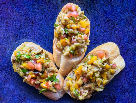 Vegetarian Bruschetta with tomatoes, eggplant, pepper and olive oil on blue plate close up