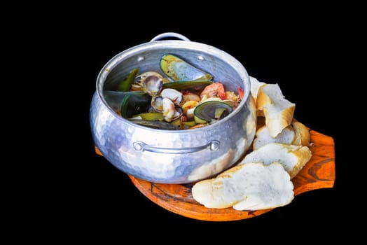 Sautéed seafood in pot close up isolated on black background side view