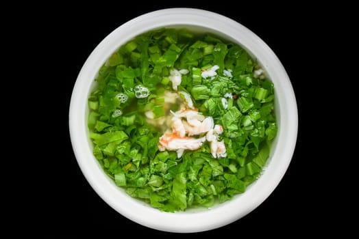 Asian soup made of spinach and seafood with shrimps isolated on black background top view
