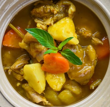Stewed chicken with potato and vegetables on blue plate isolated on black background top view