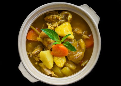 Stewed chicken with potato and vegetables on blue plate isolated on black background top view