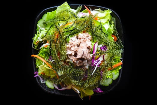 Fresh Vietnamese salad with vegetables, tuna and sea grape on black background side view