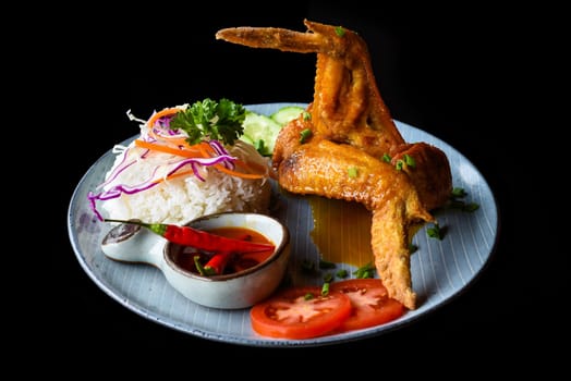 Roasted chicken wing in Vietnamese style with rice, vegetables and sauce isolated on black background top view