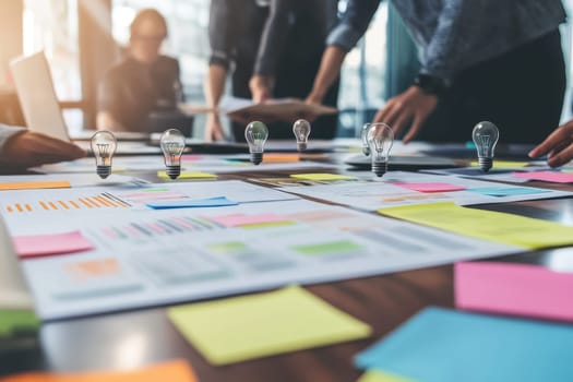 A group of people are working together on a project, with a table full of sticky notes and light bulbs. Scene is collaborative and creative, as the group is brainstorming ideas