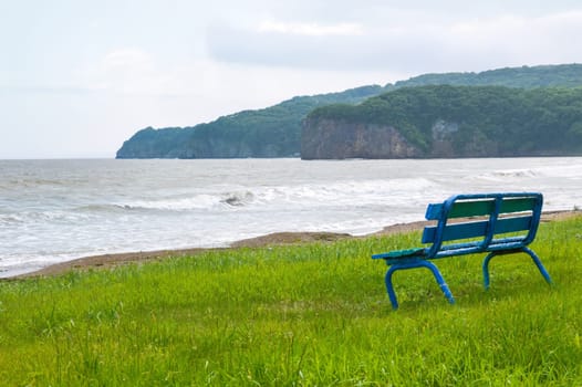 Old shabby blue bench on the shore of Japanese sea on a summer dull day before rain. No people