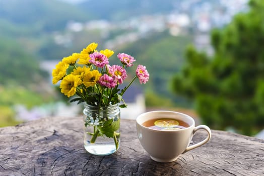 Bouquet of chrysanthemums in a vase with cup of tea with lemon and honey under sunset against the mountains of Da Lat Vietnam