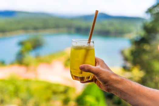 Glass of pineapple juice with ice in males hand against summer background