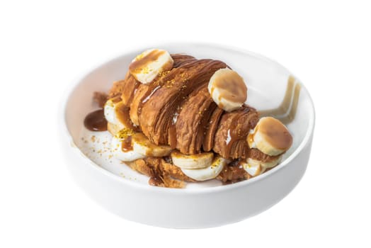 Sweet croissant with banana, salt caramel and fresh cream in white plate on white background