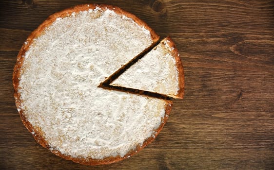 Slice of homemade pie with lemon and orange filling, covered with powdered sugar on a wooden table. copy space