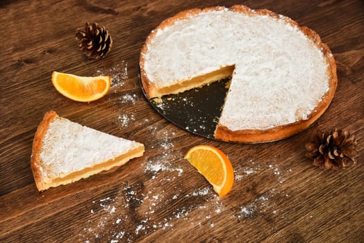 Piece of homemade pie with lemon and orange filling, covered with powdered sugar on a wooden table