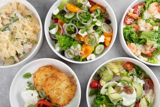 Three different vegetable salads and slavic draniki (potato pancakes) on gray marble background