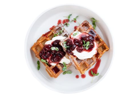 White plate with sweet belgian waffles with cream and cherry jam on a white backgroundWhite plate with sweet belgian waffles with cream and cherry jam on a white background