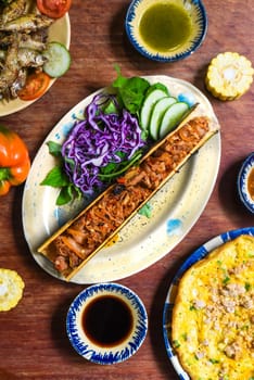 Vietnamese cuisine set made of braised deer in bamboo, fried fish, omelette with sauces on wooden table