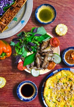 Vietnamese cuisine set made of braised deer in bamboo, fried fish, omelette with sauces on wooden table