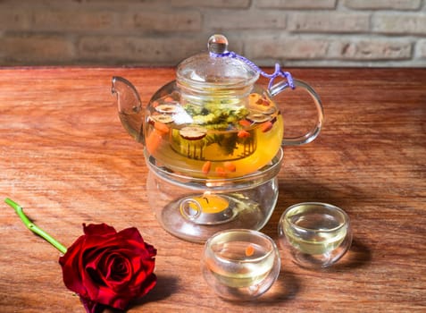 Chamomile tea with goji berries and flowers with cups and rose flower on wooden table