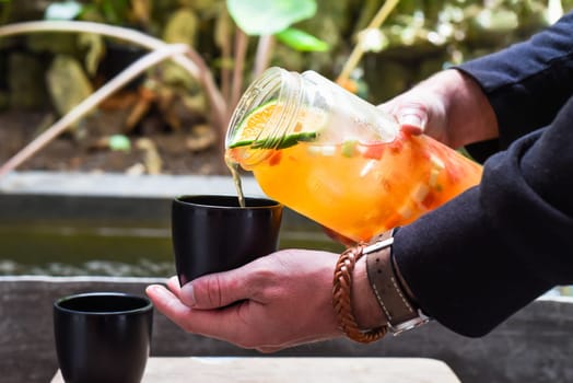 Hands holding bottle with fresh homemade juice made of oranges, watermelon, lime and pouring into a cup