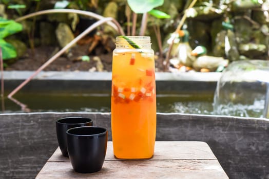 Bottle with fresh homemade juice made of oranges, watermelon, lime on the wooden table with cups