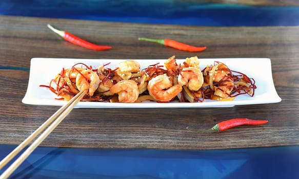 Grilled shrimp with onions and chili on a white plate on the table. For asian food menu