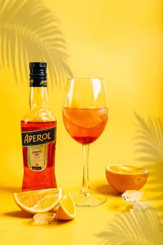 Vladivostok, Russia - 21 February 2024:  Bottle of Aperol Aperitivo summer cocktail drink with glass with spritz cocktail and oranges on bright yellow background