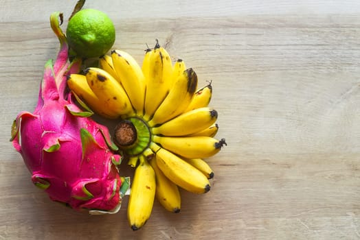 Pitaya or dragon fruit with lime and small bananas on wooden table