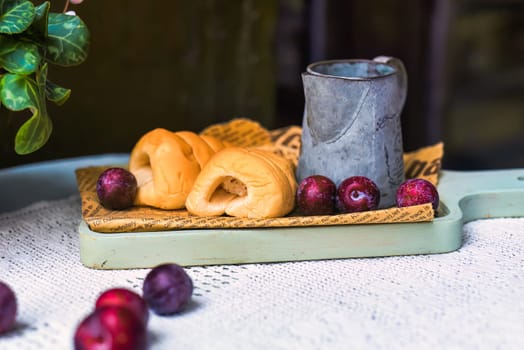 whipped cream tubes with cup and plums on wooven cloth on black background