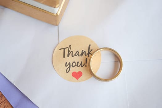 A gold ring resting on a thank you note on a table.