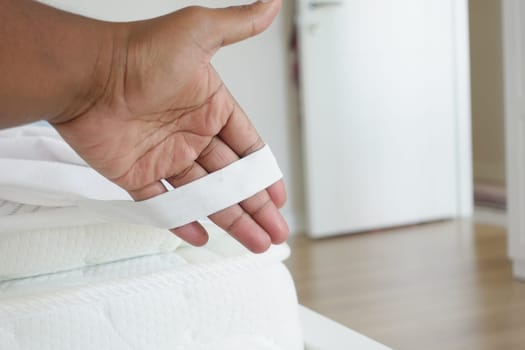 Person holds a piece of white fabric beside a bed.