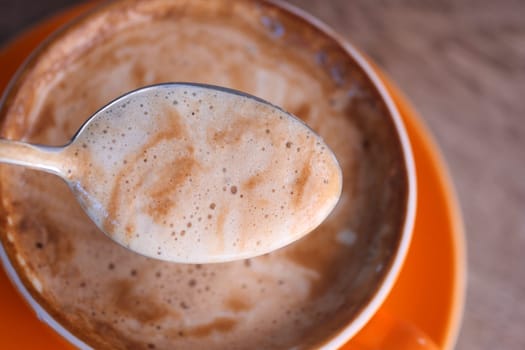 A spoonful of creamy coffee foam hovering above a cup.