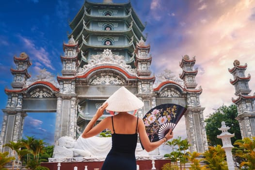 back of a female tourist in a Vietnamese Non La hat at the Da Nang pagoda in Vietnam. Travel and tourism in Asia