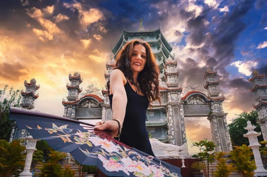 Portrait of a happy young woman tourist traveler with a fan at the temple on Buddhist pagoda in Da Nang, Vietnam. Travel and tourism in Asia