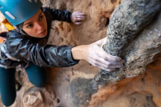Young girl is engaged in extreme sports, fearlessly climbs up the rock using white magnesia powder, holds her hand to the ledge in the relief, close-up view, focus on the finger, the girl is blurred.