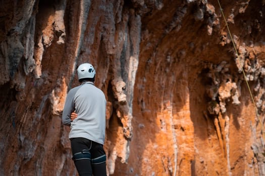 A young man stands against the background of picturesque red rocks and prepares to climb, the athlete is involved in mountaineering and leads an active lifestyle.